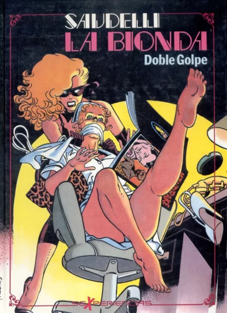 Bionda con antifaz amordaza a una mujer sentada mientras le muestra una revista erótica con las piernas abiertas.